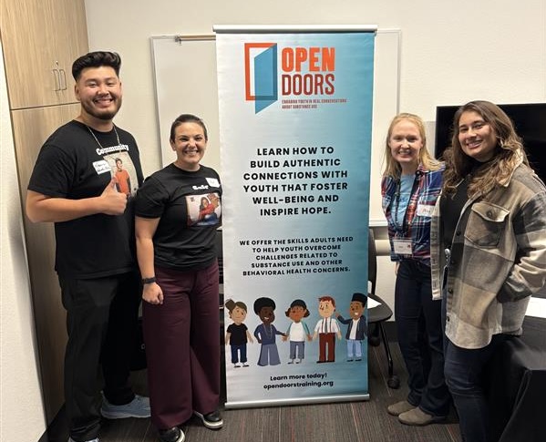 Open Doors facilitators Francisco Valverde and Kat Besse pose for a photo in front of our branded signage with staff from Saddleback Community College