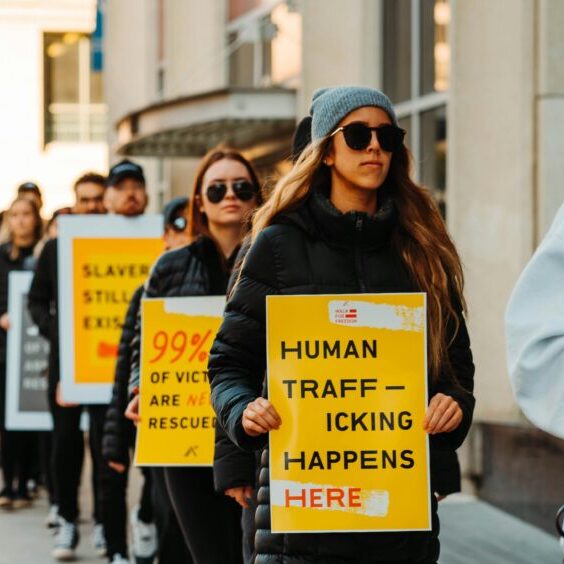 A group of people protest human trafficking. The woman in front of the line holds a sign that says "Human Trafficking Happens Here."