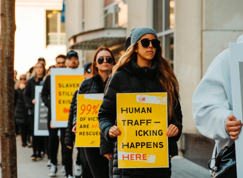 A group of people protest human trafficking. The woman in front of the line holds a sign that says "Human Trafficking Happens Here."
